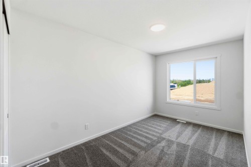 Bright room featuring a large window, neutral white walls, patterned gray carpeting, and a flush-mount ceiling light fixture - 223 157 Avenue Ne, Edmonton, AB - Indoor Photo Showing Other Room
