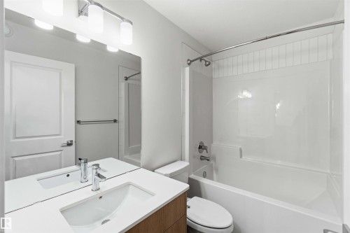 Bathroom featuring a wood-finish vanity with an integrated sink and chrome faucet, a large mirror, and a white tub with a shower kit - 223 157 Avenue Ne, Edmonton, AB - Indoor Photo Showing Bathroom
