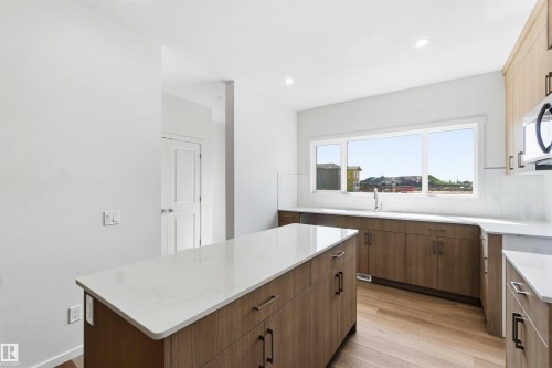 Modern kitchen featuring a central island with a light-toned countertop, wood-finish cabinetry, and stainless steel appliances - 223 157 Avenue Ne, Edmonton, AB - Indoor Photo Showing Kitchen