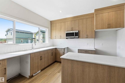 Modern kitchen featuring a light wood-finish cabinetry, a large window, white subway tile backsplash, white countertops, and wood-finish flooring - 223 157 Avenue Ne, Edmonton, AB - Indoor Photo Showing Kitchen