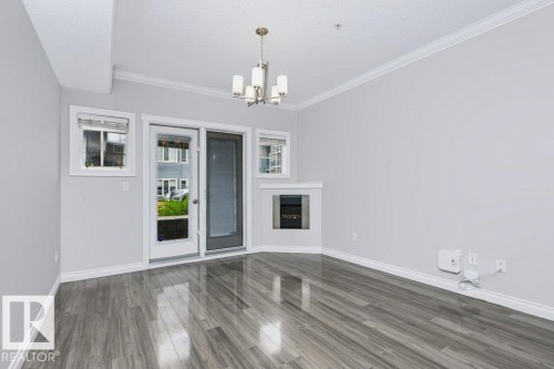 Expansive room featuring wood-finish flooring, a built-in fireplace, crown molding, and a modern chandelier - #137 10121 80 Av Nw, Edmonton, AB - Indoor With Fireplace