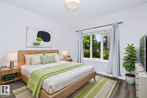 Spacious bedroom featuring light wood-finish flooring, a large window, white walls, and a ceiling-mounted light fixture - #137 10121 80 Av Nw, Edmonton, AB - Indoor Photo Showing Bedroom