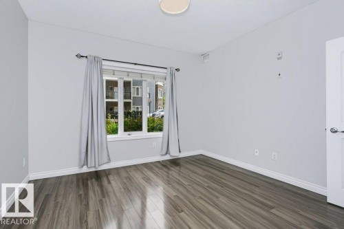 Spacious interior featuring wood-finish flooring, light grey walls, white trim, and a contemporary ceiling light fixture - #137 10121 80 Av Nw, Edmonton, AB - Indoor Photo Showing Other Room