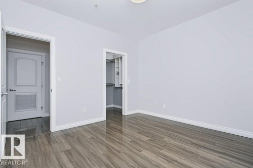 Spacious interior featuring wood-finish flooring, light gray walls, white trim, and a walk-in closet with built-in shelving - #137 10121 80 Av Nw, Edmonton, AB - Indoor Photo Showing Other Room