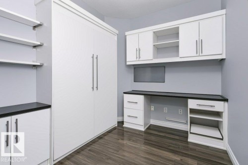 Built-in desk and cabinetry with a dark countertop, white storage units, and wood-finish flooring - #137 10121 80 Av Nw, Edmonton, AB - Indoor Photo Showing Other Room