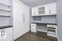 Built-in desk and cabinetry with a dark countertop, white storage units, and wood-finish flooring - 