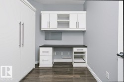 Integrated built-in desk and shelving unit with white cabinetry, dark countertop, and dark wood-finish flooring - 