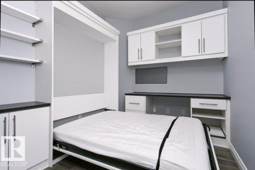 Murphy bed system featuring built-in cabinetry, floating shelves, integrated desk, and dark countertops - #137 10121 80 Av Nw, Edmonton, AB - Indoor Photo Showing Bedroom