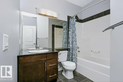 Bathroom featuring a dark wood-finish vanity with an undermount sink, dark countertop, and large mirror - #137 10121 80 Av Nw, Edmonton, AB - Indoor Photo Showing Bathroom