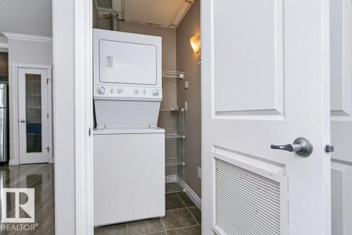 Built-in laundry closet featuring a stacked washer and dryer, tiled flooring, and wall-mounted shelving - #137 10121 80 Av Nw, Edmonton, AB - Indoor Photo Showing Laundry Room