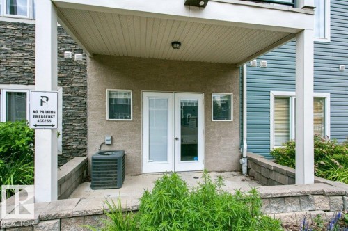 Ground-level patio with stucco exterior, double glass panel door, air conditioning unit, and a stone-clad wall accent - #137 10121 80 Av Nw, Edmonton, AB - Outdoor With Exterior