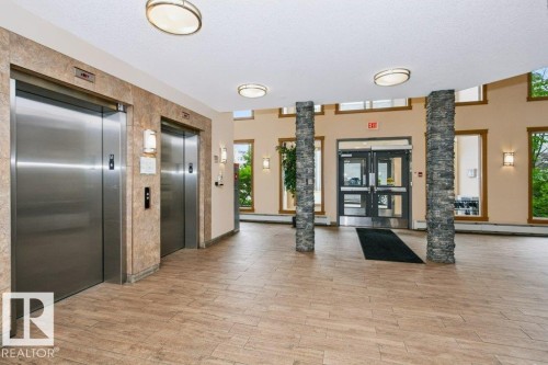 Entry foyer featuring tile flooring, stone-clad columns, and dual stainless steel elevators - #137 10121 80 Av Nw, Edmonton, AB - Indoor Photo Showing Other Room