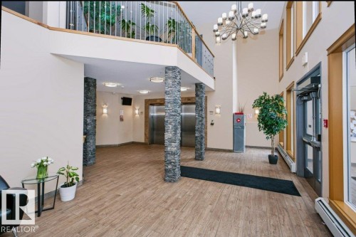 Spacious lobby featuring wood-finish flooring, stacked stone columns, a multi-story ceiling, and a prominent chandelier - #137 10121 80 Av Nw, Edmonton, AB - Indoor Photo Showing Other Room