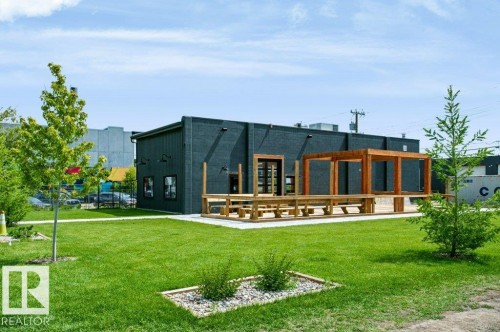 Modern commercial building featuring a dark facade, an expansive wood-finish deck, a coordinating wood pergola, and integrated exterior lighting - #137 10121 80 Av Nw, Edmonton, AB - Outdoor