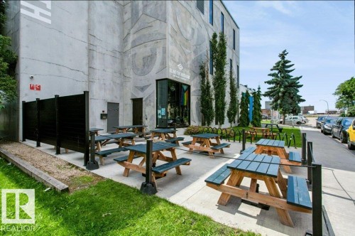 Exterior patio area featuring multiple picnic tables with benches, a black privacy fence, and concrete paving - #137 10121 80 Av Nw, Edmonton, AB - Outdoor