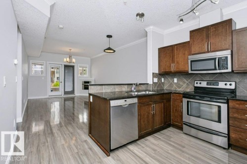 Kitchen featuring wood cabinetry, stainless steel appliances, dark countertops, and a tiled backsplash - #137 10121 80 Av Nw, Edmonton, AB - Indoor Photo Showing Kitchen With Stainless Steel Kitchen