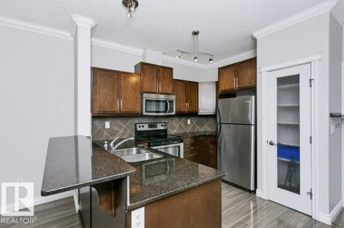 Modern kitchen featuring wood cabinetry, stainless steel appliances, dark granite countertops, and a tile backsplash - #137 10121 80 Av Nw, Edmonton, AB - Indoor Photo Showing Kitchen With Stainless Steel Kitchen With Double Sink With Upgraded Kitchen