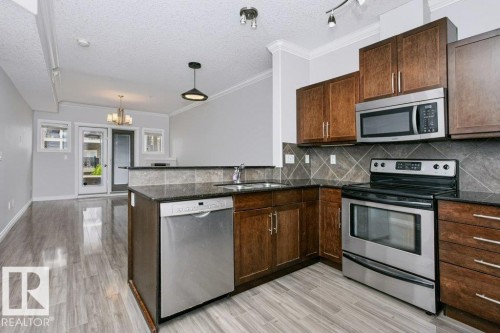 Well-appointed kitchen featuring wood-finish cabinetry, stainless steel appliances, dark stone countertops, and a tiled backsplash - #137 10121 80 Av Nw, Edmonton, AB - Indoor Photo Showing Kitchen With Stainless Steel Kitchen