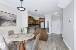 Open-concept dining and kitchen area featuring wood-finish flooring, crown molding, a kitchen island with seating, a white paneled entry door, and stainless steel appliances - 