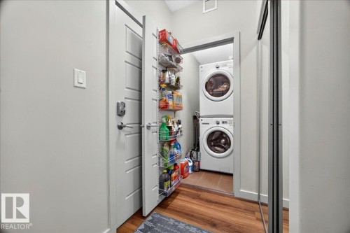 Dedicated laundry closet featuring a stacked washer and dryer, wood-finish flooring, and a door-mounted shelving system - 106 320 Ambleside Link Sw, Edmonton, AB - Indoor Photo Showing Laundry Room
