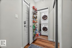 Dedicated laundry closet featuring a stacked washer and dryer, wood-finish flooring, and a door-mounted shelving system - 