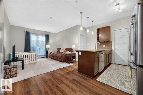 Open-concept living area featuring wood-finish flooring, a kitchen island with stone countertop, stainless steel appliances, and pendant lighting - 106 320 Ambleside Link Sw, Edmonton, AB - Indoor Photo Showing Kitchen
