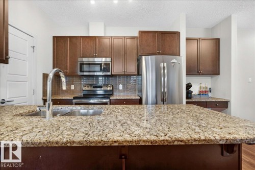 Kitchen island with stone-finish countertop and undermount stainless steel sink featuring a gooseneck faucet - 106 320 Ambleside Link Sw, Edmonton, AB - Indoor Photo Showing Kitchen With Double Sink With Upgraded Kitchen