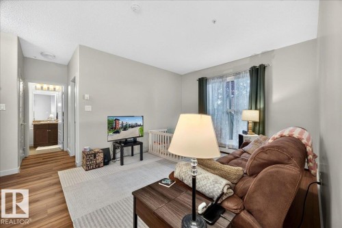 Open-concept living space featuring wood-finish flooring, light grey wall tones, and a large window with privacy sheers - 106 320 Ambleside Link Sw, Edmonton, AB - Indoor Photo Showing Living Room