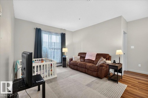 Bright interior space featuring light gray walls and wood-finish flooring - 106 320 Ambleside Link Sw, Edmonton, AB - Indoor Photo Showing Living Room