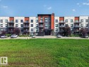 Contemporary multi-story building featuring a facade with white, gray, and orange accents - 106 320 Ambleside Link Sw, Edmonton, AB  - Outdoor With Balcony 