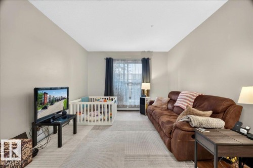 Living area featuring light neutral wall tones, window with vertical blinds, and light-toned carpet flooring - 106 320 Ambleside Link Sw, Edmonton, AB - Indoor