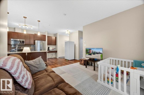 Open-concept living space featuring wood-finish flooring, a kitchen with dark cabinetry, stainless steel appliances, and pendant lighting - 106 320 Ambleside Link Sw, Edmonton, AB - Indoor