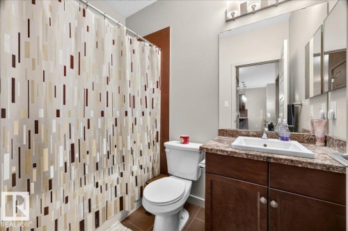 Bathroom featuring a brown wood-finish vanity with a light-colored countertop, an undermount sink, and a wall-mounted mirror - 106 320 Ambleside Link Sw, Edmonton, AB - Indoor Photo Showing Bathroom