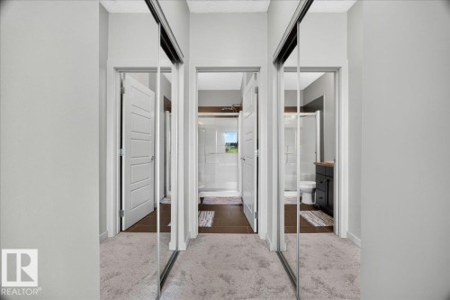 Mirrored sliding closet doors reflecting a modern bathroom with a glass-enclosed shower, dark wood-finish vanity, and wood-finish flooring - 106 320 Ambleside Link Sw, Edmonton, AB - Indoor Photo Showing Other Room