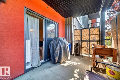 Covered balcony with concrete flooring, vibrant red exterior wall, and sliding glass door access - 106 320 Ambleside Link Sw, Edmonton, AB -  Photo Showing Other Room