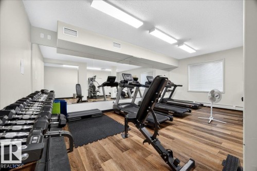 Fitness room featuring wood-finish flooring, full-wall mirrors, and bright overhead lighting - 106 320 Ambleside Link Sw, Edmonton, AB - Indoor Photo Showing Gym Room