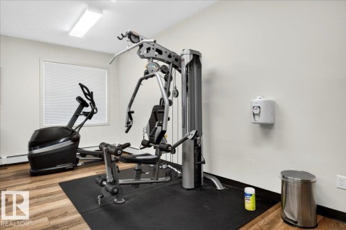 Dedicated fitness area featuring wood-finish flooring, a multi-station weight machine, and a cardio machine - 106 320 Ambleside Link Sw, Edmonton, AB - Indoor Photo Showing Gym Room