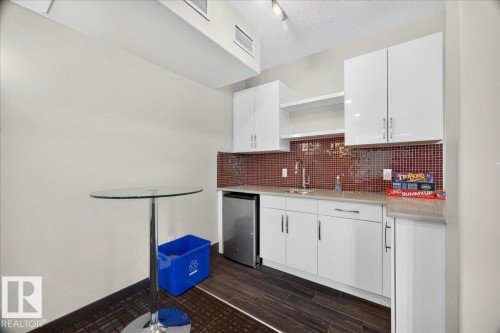 Kitchenette featuring white cabinetry, a red mosaic tile backsplash, a stainless steel sink, and wood-finish flooring - 106 320 Ambleside Link Sw, Edmonton, AB - Indoor Photo Showing Kitchen