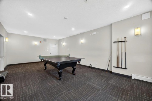 Spacious recreational area featuring a billiard table with a ping-pong conversion top, patterned dark carpet flooring, recessed lighting, and wall-mounted sconces - 106 320 Ambleside Link Sw, Edmonton, AB - Indoor Photo Showing Other Room