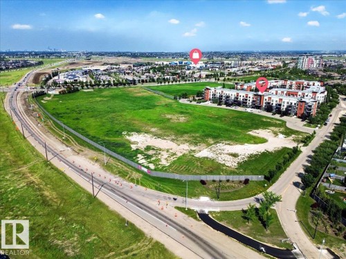 Expansive undeveloped land parcel with surrounding residential and commercial structures - 106 320 Ambleside Link Sw, Edmonton, AB - Outdoor With View