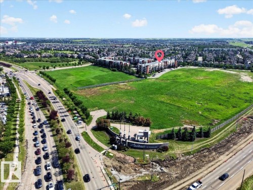 Contemporary multi-story building featuring a red-orange facade accent, situated near a substantial green space - 106 320 Ambleside Link Sw, Edmonton, AB - Outdoor With View