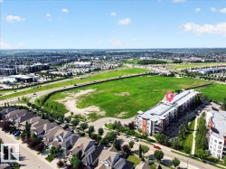 Modern multi-story building featuring a flat roof and balconies, situated alongside a roadway and expansive green space - 