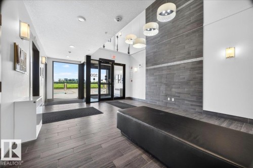 Lobby area featuring wood-finish tile flooring, a dark accent wall with horizontal tile, and multiple contemporary pendant light fixtures - 106 320 Ambleside Link Sw, Edmonton, AB - Indoor Photo Showing Other Room