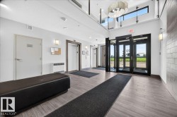Modern building entrance featuring wood-finish flooring, glass entry doors, and a two-story ceiling with a contemporary chandelier - 