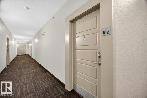 Entry door with horizontal panel design and contemporary hardware opening onto a hallway featuring patterned carpet flooring, recessed ceiling lights, and wall sconces - 106 320 Ambleside Link Sw, Edmonton, AB - Indoor Photo Showing Other Room