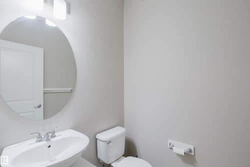 Bathroom featuring a pedestal sink with chrome faucet, circular mirror, and two-bulb vanity light fixture - 17707 59 Street Nw, Edmonton, AB - Indoor Photo Showing Bathroom