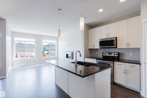 Modern kitchen featuring a large island with a double sink, white cabinetry, granite countertops, and stainless steel appliances - 17707 59 Street Nw, Edmonton, AB - Indoor Photo Showing Kitchen With Upgraded Kitchen