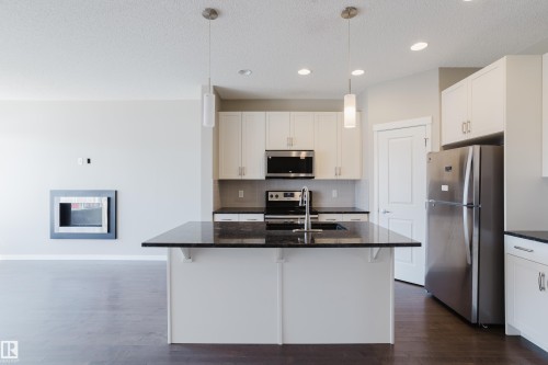 Open-concept kitchen featuring an island with a dark countertop and pendant lighting, white cabinetry, stainless steel appliances, and wood-finish flooring - 17707 59 Street Nw, Edmonton, AB - Indoor Photo Showing Kitchen With Stainless Steel Kitchen With Double Sink With Upgraded Kitchen