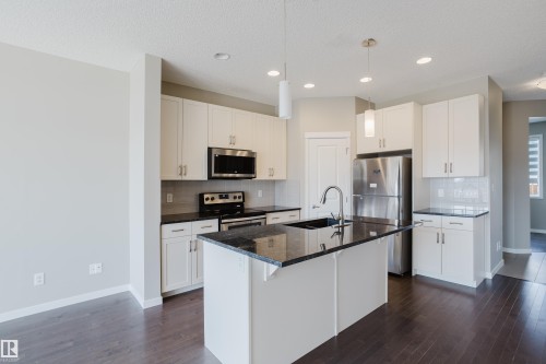 Modern kitchen featuring dark granite countertops, stainless steel appliances, white cabinetry, and wood-finish flooring - 17707 59 Street Nw, Edmonton, AB - Indoor Photo Showing Kitchen With Stainless Steel Kitchen With Upgraded Kitchen