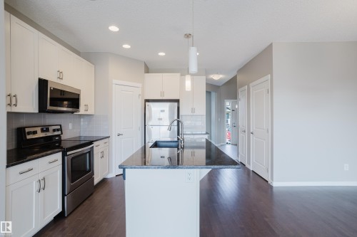 Modern kitchen featuring white cabinetry, stainless steel appliances, dark stone countertops, and wood-finish flooring - 17707 59 Street Nw, Edmonton, AB - Indoor Photo Showing Kitchen With Stainless Steel Kitchen With Upgraded Kitchen